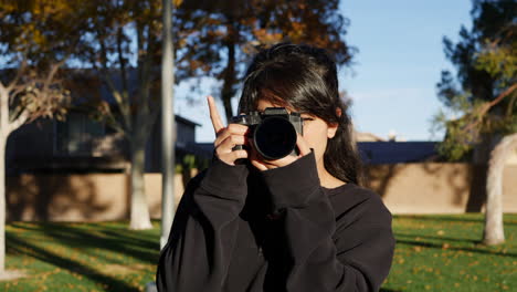 una fotógrafa caliente feliz y sonriente en hojas de otoño al atardecer tomando fotos con una cámara digital en cámara lenta