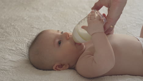 Mano-De-La-Madre-Sosteniendo-El-Biberón-De-Leche-Alimentación-Del-Bebé-Recién-Nacido,-Tiempo-De-Vinculación-Dormitorio-Blanco