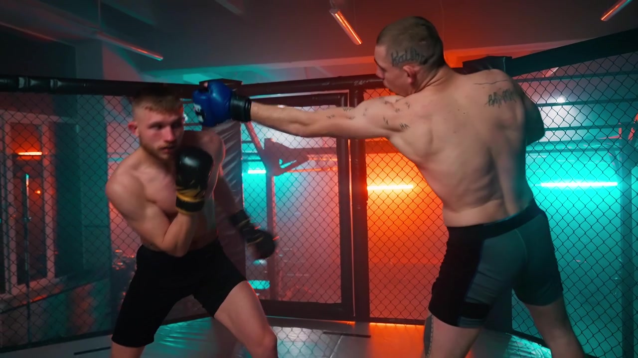 ドラマチックなネオン照明の下、MMAケージ内でスパーリングする2人の男性ファイター