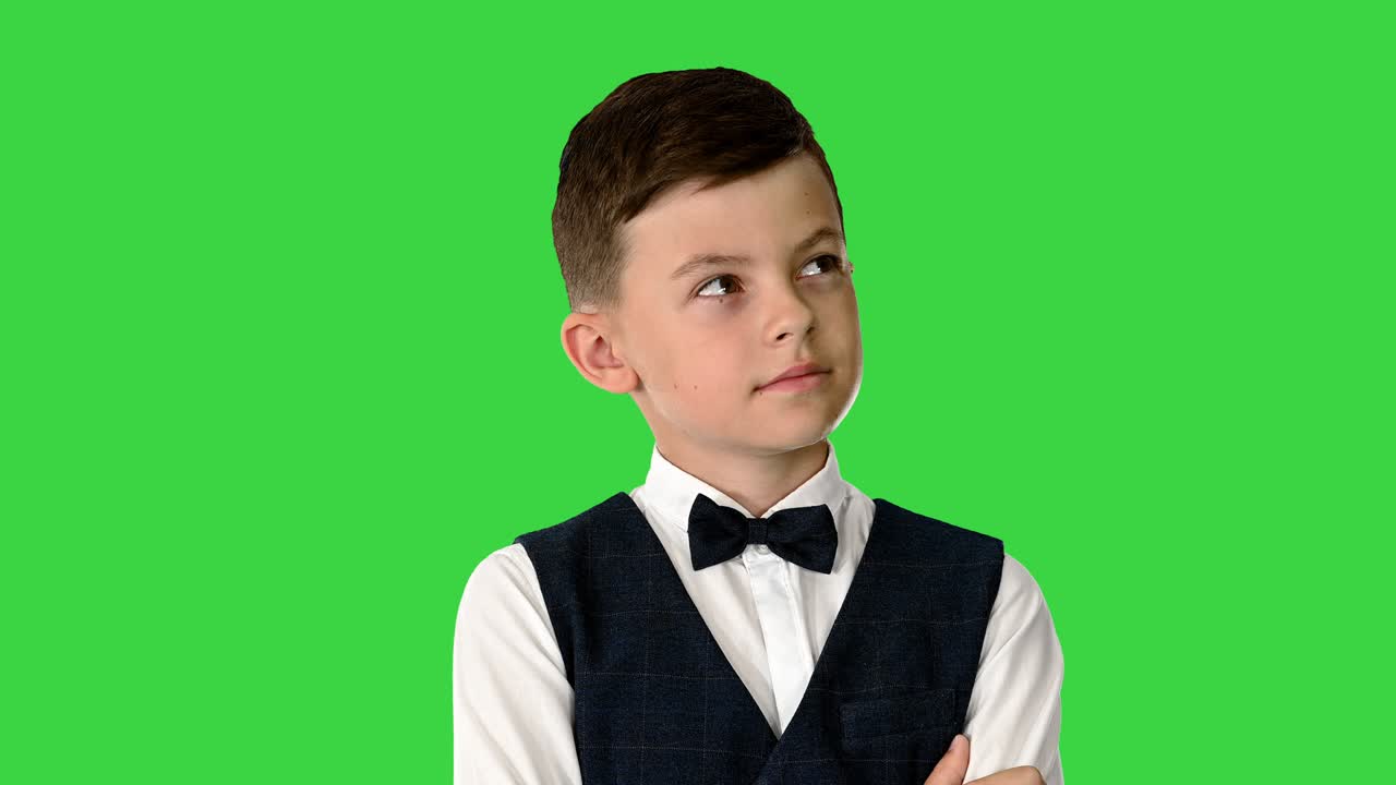 niño pequeño con una corbata de papagaio de pie con los brazos cruzados y mirando hacia arriba pensando en una pantalla verde, clave de croma
