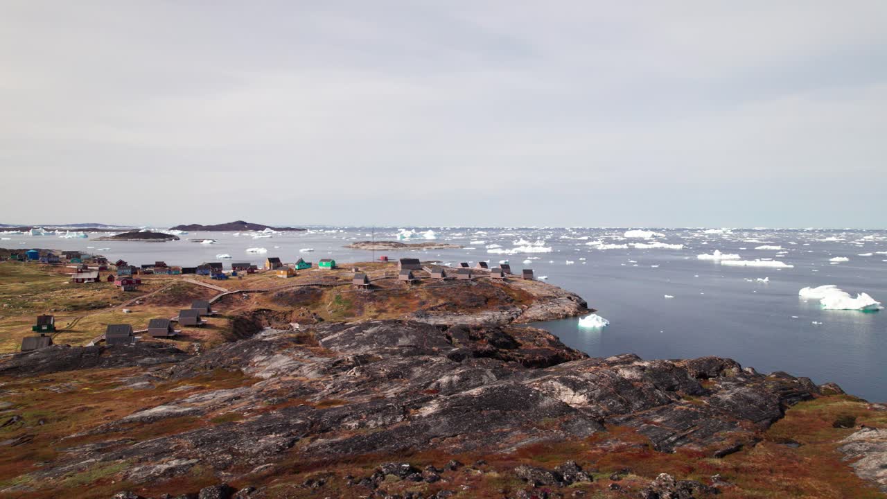 Sideways dolly drone shot capturing the coastal Greenlandic settlement of Ilimanaq, surrounded by Arctic mountains and icy seascapes