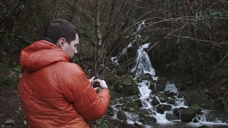 hombre tomando una foto de una cascada en un bosque