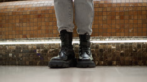 low angle close up shot showing female client gliding black leather boot over tiled bench seat in modern shopping mall near illuminated fountain, highlighting stylish movement and footwear detail