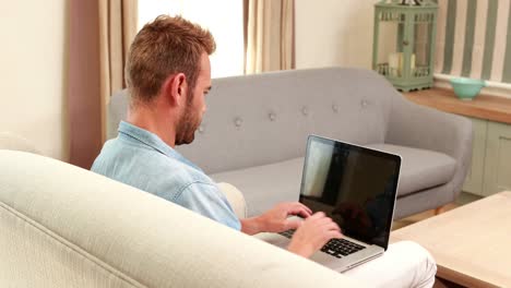 hombre guapo en el sofá usando una computadora portátil