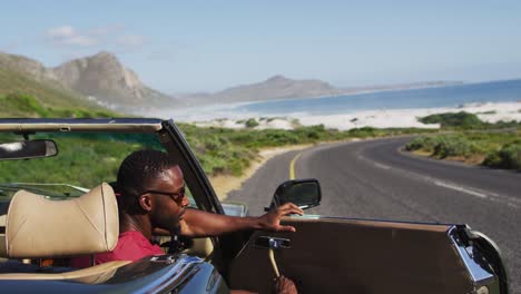 african american man wearing sunglasses stepping out of convertible car on road