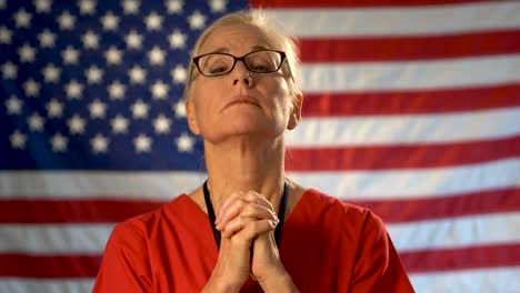 medium tight portrait of a healthcare nurse looking concerned and praying with an out of focus american flag