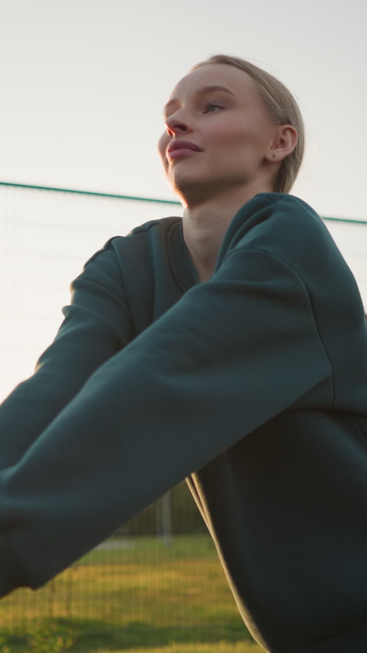 joven con capucha verde jugando al voleibol con otro jugador en el fondo, con efecto de brillo de la luz solar en la distancia, en contra de un campo abierto y un edificio en el fondo durante la hora de oro