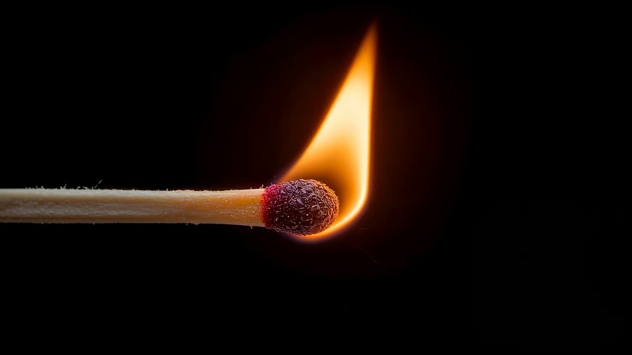 Striking red-tipped match head igniting flame, growing blue base and charring for study in studio