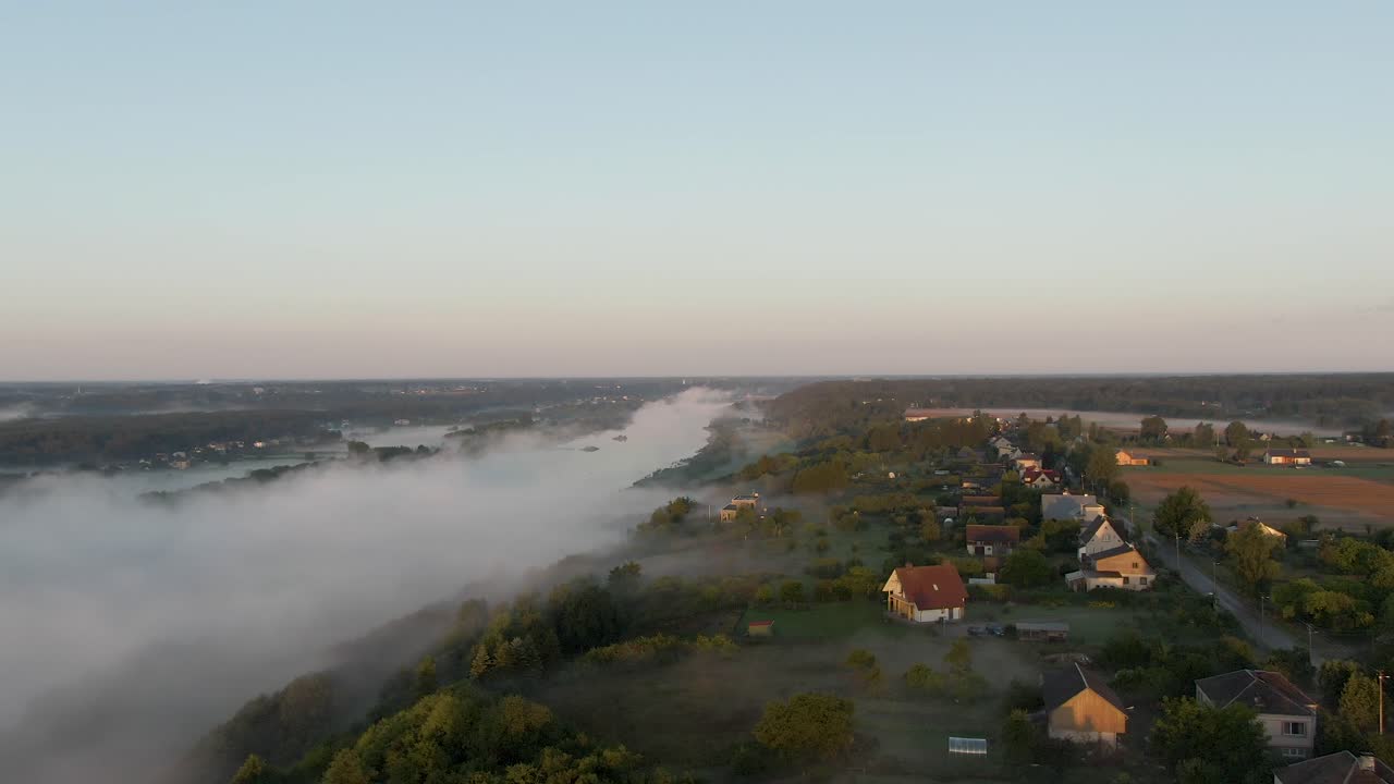 Side aerial shot of small Lithuanian country houses while flying towards river Nemunas in the foggy early morning