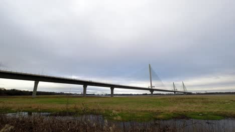 Time-lapse-clouds-passing-and-traffic-rush-over-rural-countryside-marshland-suspension-bridge-at-speed