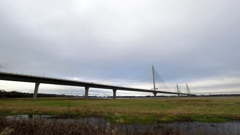 Nubes-De-Lapso-De-Tiempo-Que-Pasan-Y-El-Tráfico-Se-Precipita-Sobre-El-Puente-Colgante-De-Marismas-Rurales-A-Gran-Velocidad