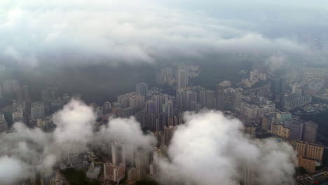 Aerial view of dense Hong Kong cityscape under foggy twilight, featuring high-rise buildings, residential towers, harbor, and mountains in the background