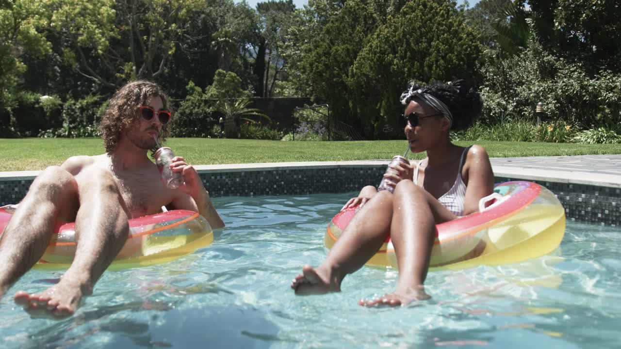 una pareja diversa, un hombre caucásico y una mujer afroamericana, disfrutan de la piscina.