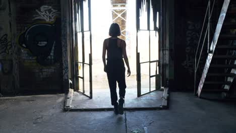 woman in grunge fashion clothing walking towards exit of a rundown warehouse - medium shot