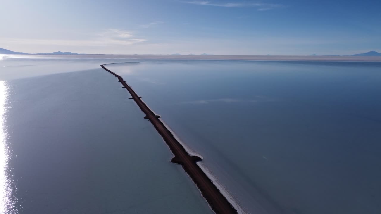 Aerial: Narrow road extends into vast shallow salt lake, Uyuni Bolivia