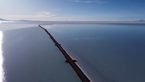 aerial: narrow road extends into vast shallow salt lake, uyuni bolivia