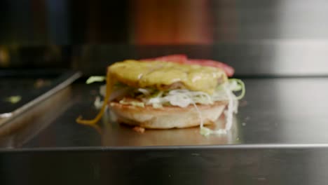 beef patty with cheese placed on burger bun with vegetables, close-up