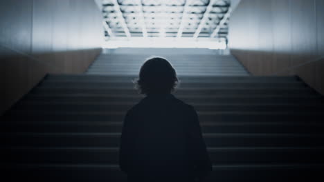 Teenager silhouette going upstairs alone on light. Teen student walk stairway.