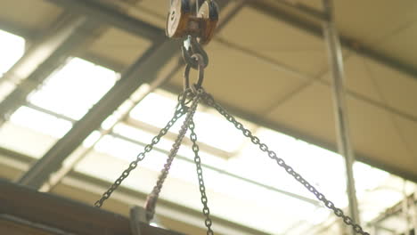 Tilt-up-shot-of-a-hanging-rusty-heavy-steal-structure-lifting-up-by-a-hoist-high-in-the-bright-daylight,-part-of-a-manufacturing-processus-inside-an-industrial-hall