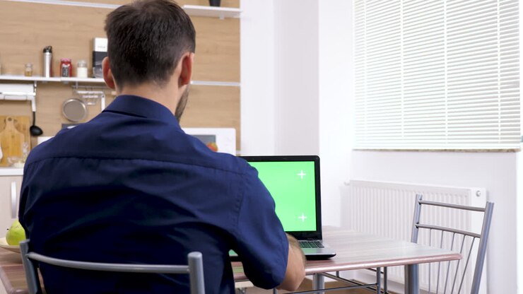 Man using laptop with green screen in kitchen