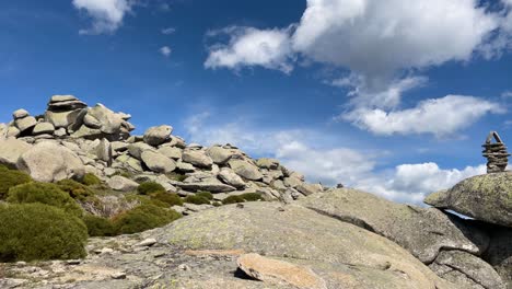 Vemos-En-Un-Pico-Una-Gran-Acumulación-De-Piedras-De-Granito-De-Diferentes-Tamaños-Y-En-Una-Gran-Roca-Aparece-Un-Hito-Formado-Por-Pequeñas-Piedras,-Las-2-últimas-Formando-Un-Pico-Con-Un-Cielo-Azul-Con-Nubes.