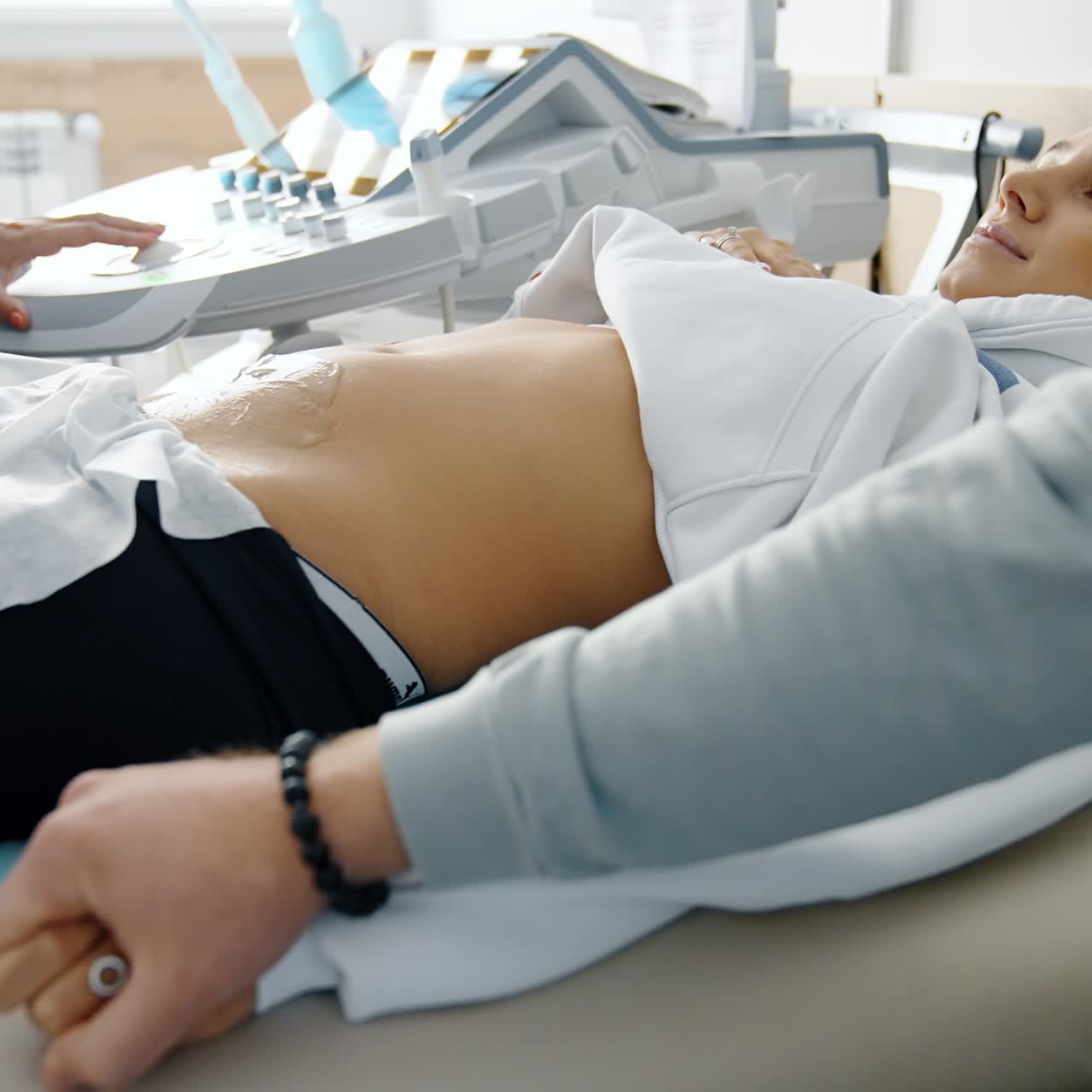 Beautiful pregnant lady undergoing ultrasound examination. Male hand takes his wife's hand showing love and support