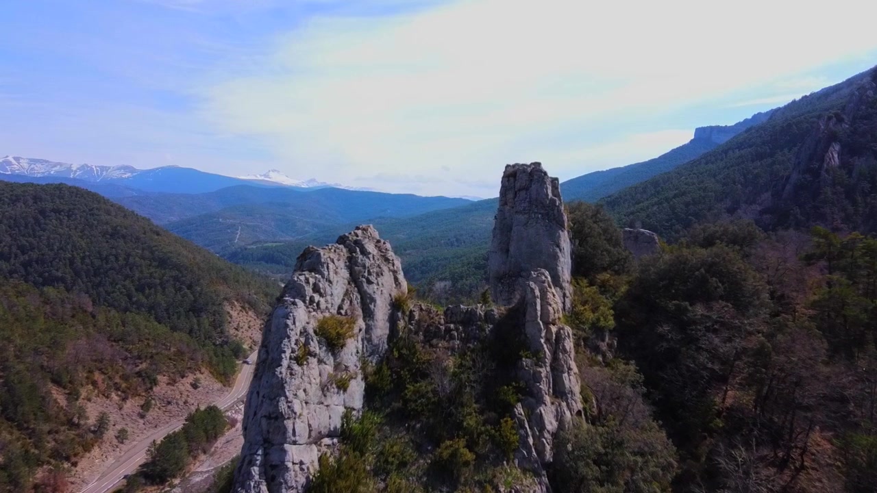Flugaufnahme zwischen Felsen in den Bergen der spanischen Pyrenäen, mit bewölktem Himmel und schneebedeckten Bergen im Hintergrund