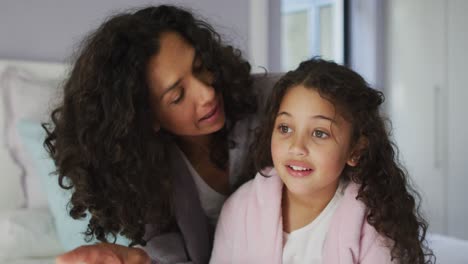 Mixed-race-mother-and-daughter-sitting-in-bedroom-and-looking-at-something