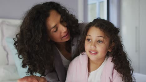 mixed race mother and daughter sitting in bedroom and looking at something