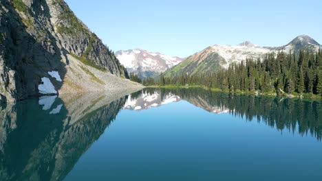 Flying-over-the-lake-glassy-surface-between-mountains-at-sunrise