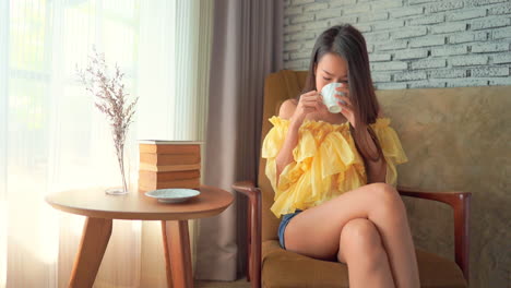 一位年輕好看的女人喝咖啡或茶,在家裡坐在椅子上放鬆時微笑著