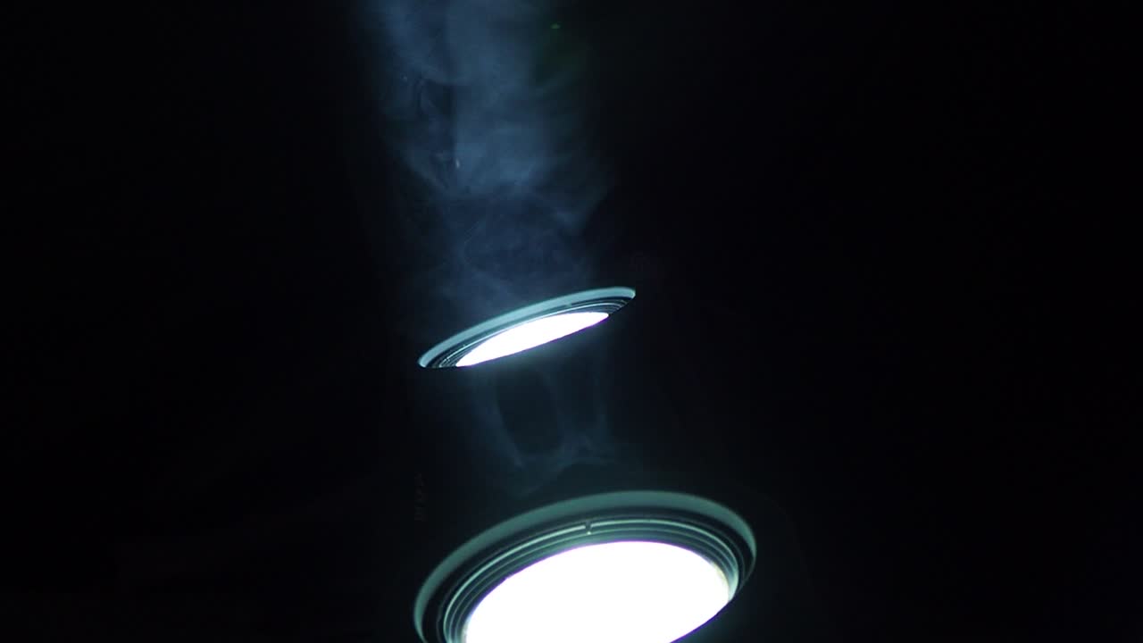 primer plano de dos focos led blancos que brillan hacia arriba con humo volando a través del haz de luz, con espacio de copia