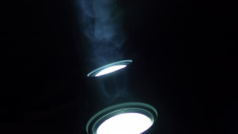 Close-up-shot-of-two-white-LED-spotlights-shining-light-upwards-with-smoke-flying-through-the-light-beam,-with-copy-space