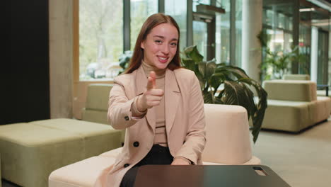 portrait of caucasian young businesswoman pointing to camera selecting hire sitting in office lobby