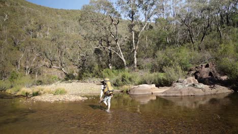 a hiker walks accross a river with a pack on the victorian high country