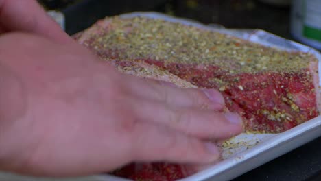 two hands rub spices and salt into a thick raw rib eye steak prepping it to be grilled