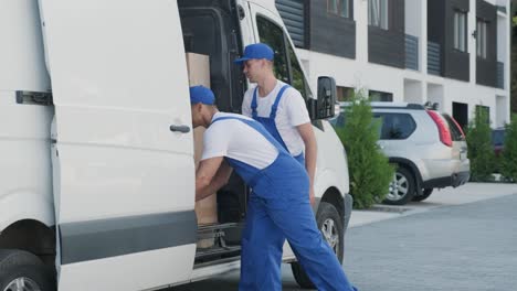 two young workers of removal company are loading boxes and furniture into a minibus