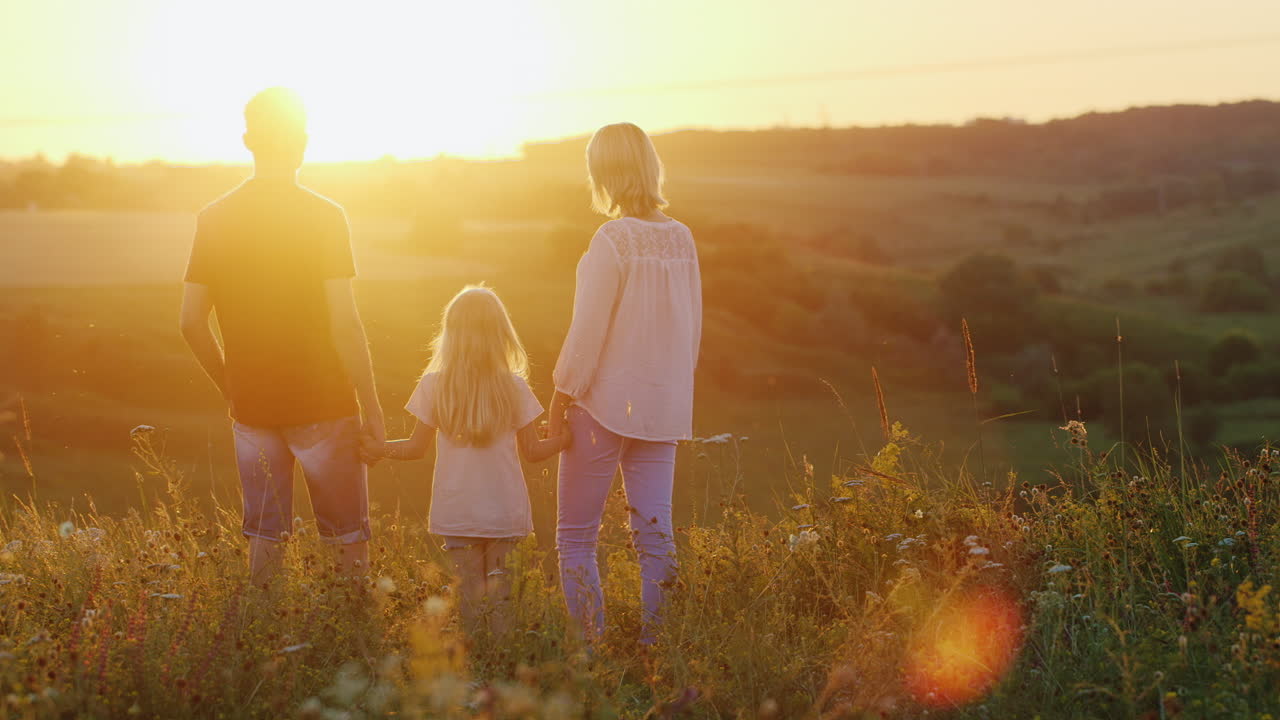 Giovane famiglia di tre persone che si gode il tramonto su una scogliera.