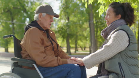 woman talking with old man in wheelchair in park