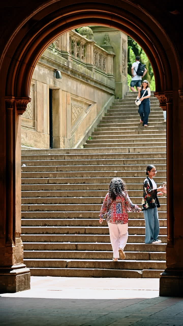 New York, USA, 8 agosto 2025: Persone che salgono una scalinata in pietra, viste attraverso un arco a Bethesda Terrace. Veduta architettonica attraverso un arco in pietra di persone che salgono le scale a Central Park.