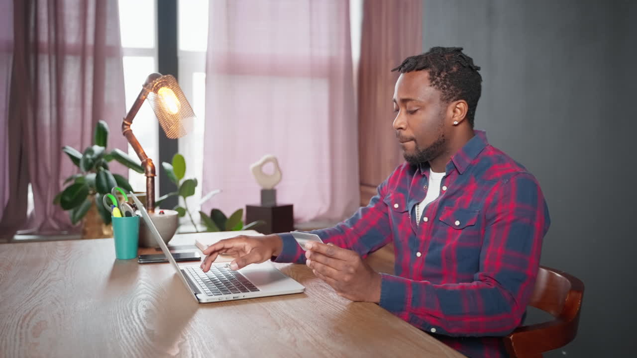 Man working from home, checking credit card on laptop