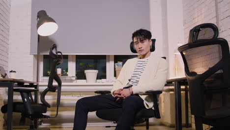 confident young man sitting on office chair and looking at camera