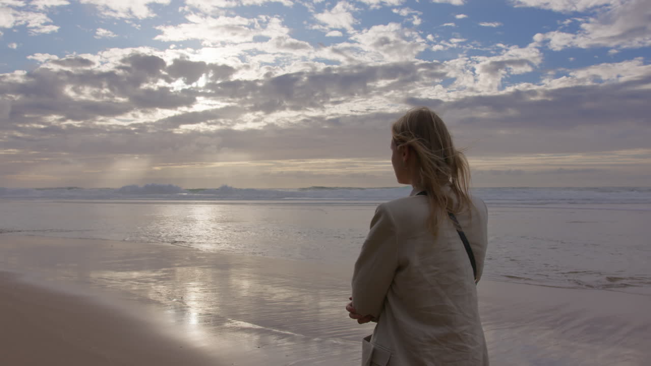 해가 지는 해변에 서서 바다를 바라보는 여자