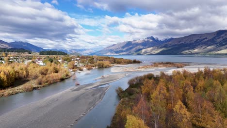 drone captures vibrant autumn foliage and serene river in glenorchy, new zealand. bright daylight enhances the scenic mountain backdrop