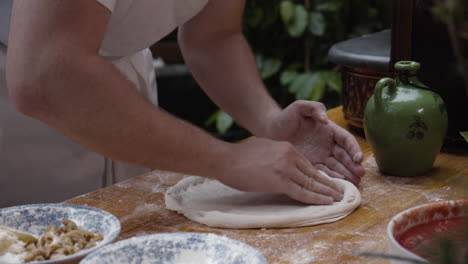 el chef estira y forma la masa de pizza en un círculo sobre una mesa de cocina de madera