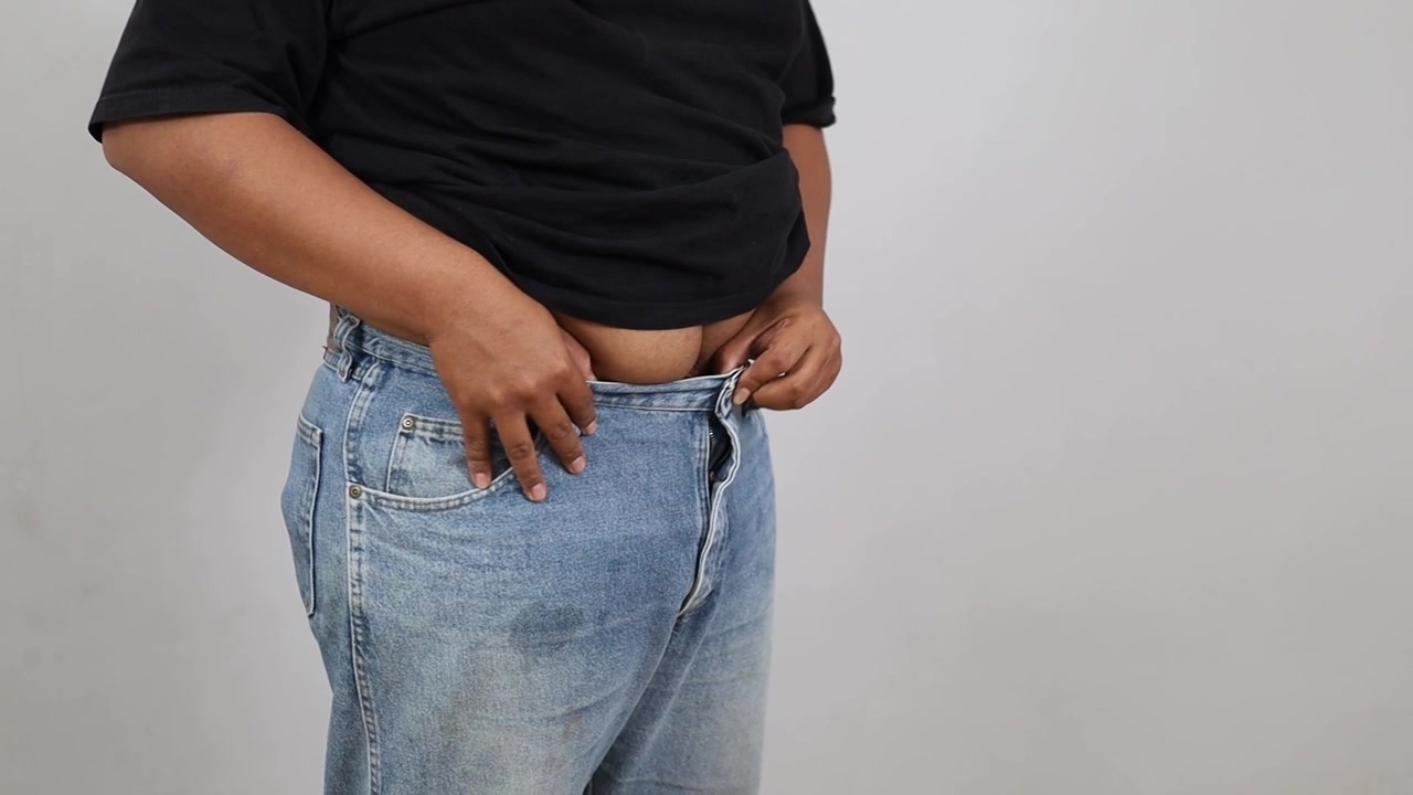 Asian Plus-size man buttoning oversized pants, celebrating weight loss. dieting result. Close up