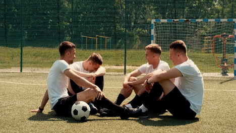 young street football players sitting on pitch, resting and supporting each other