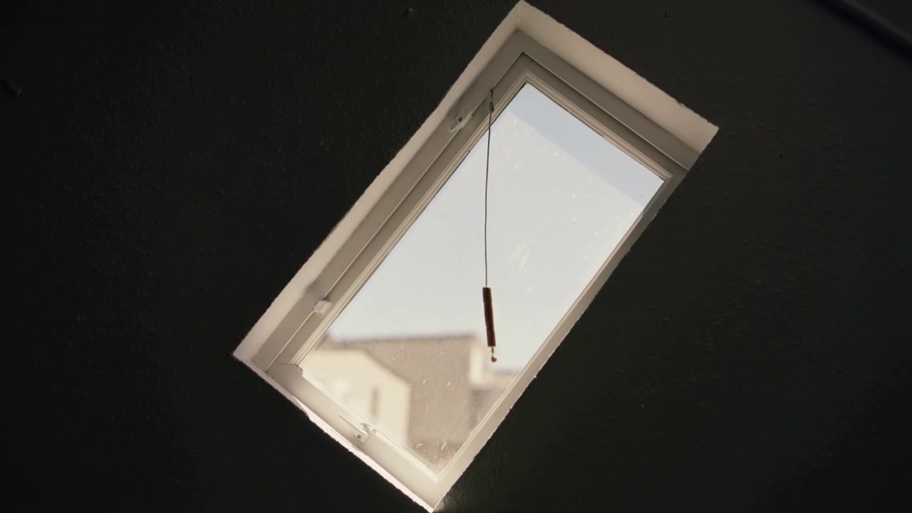 Swaying thin pull cord signaling small draft moving through skylight in attic room, showing dust