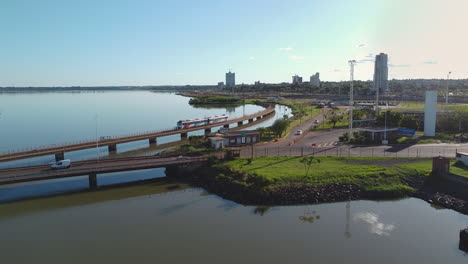 A-cityscape-containing-a-train-crossing-over-the-Rio-Parana-River,-Puente-Internacional-Posadas---Encarnación-and-cars-driving-on-the-bridge