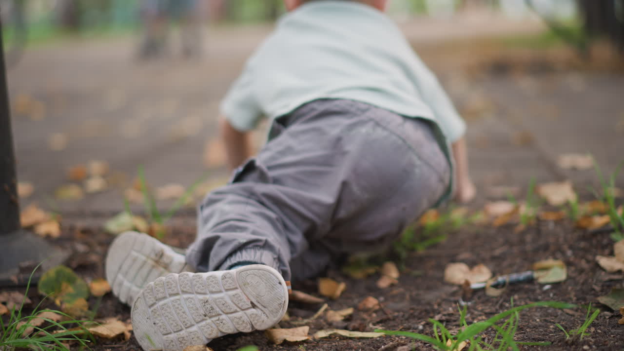 Il bambino continua a gattonare. Bambino piccolo in continuo movimento dopo una caduta. Bambino piccolo che avanza con insistenza dopo un inciampo al parco. Bambino piccolo che gattona ripetutamente dopo essere inciampato in un'area del parco